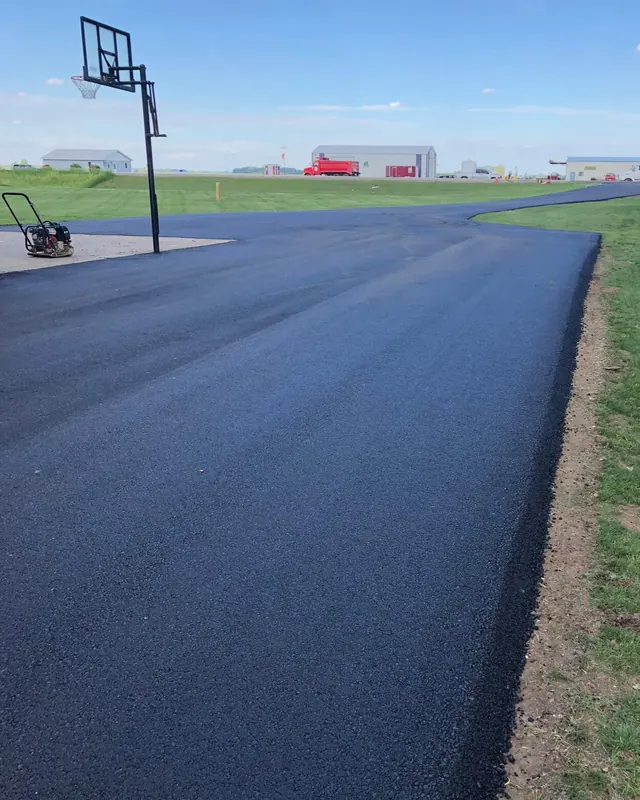 Long new asphalt driveway beside a lawn